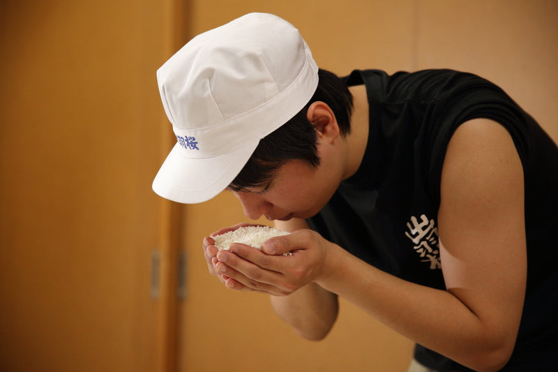 A Dewazakura brewer smelling rice held in his cupped hands.