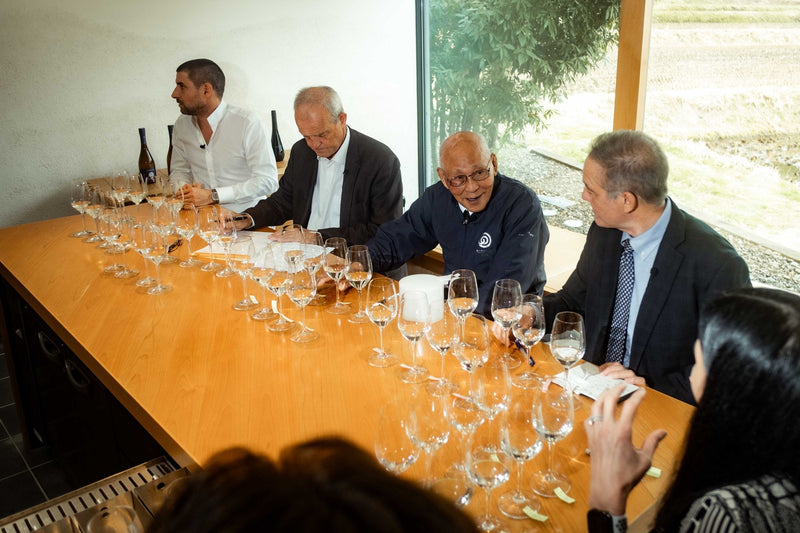 Participants at a tasting table lined with wine glasses.
